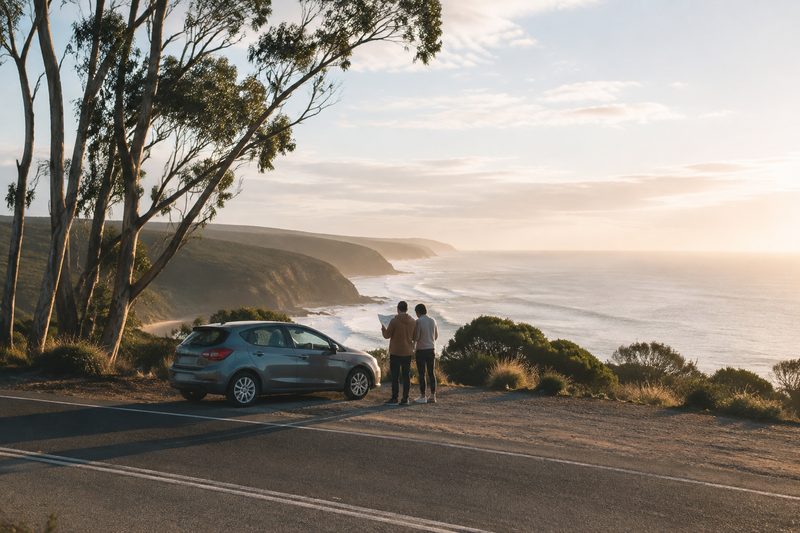 Travellers checking a map beside a car at a coastal lookout